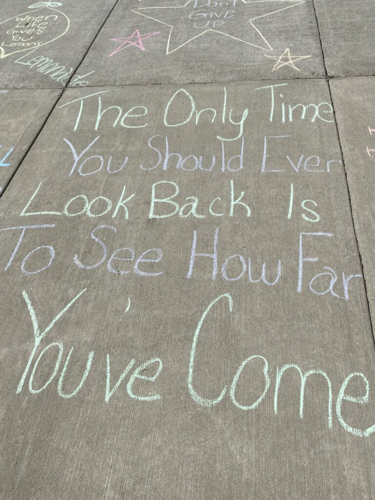 Message written in sidewalk chalk reads: "The Only Time You Should Ever Look Back Is To See How Far You've Come"